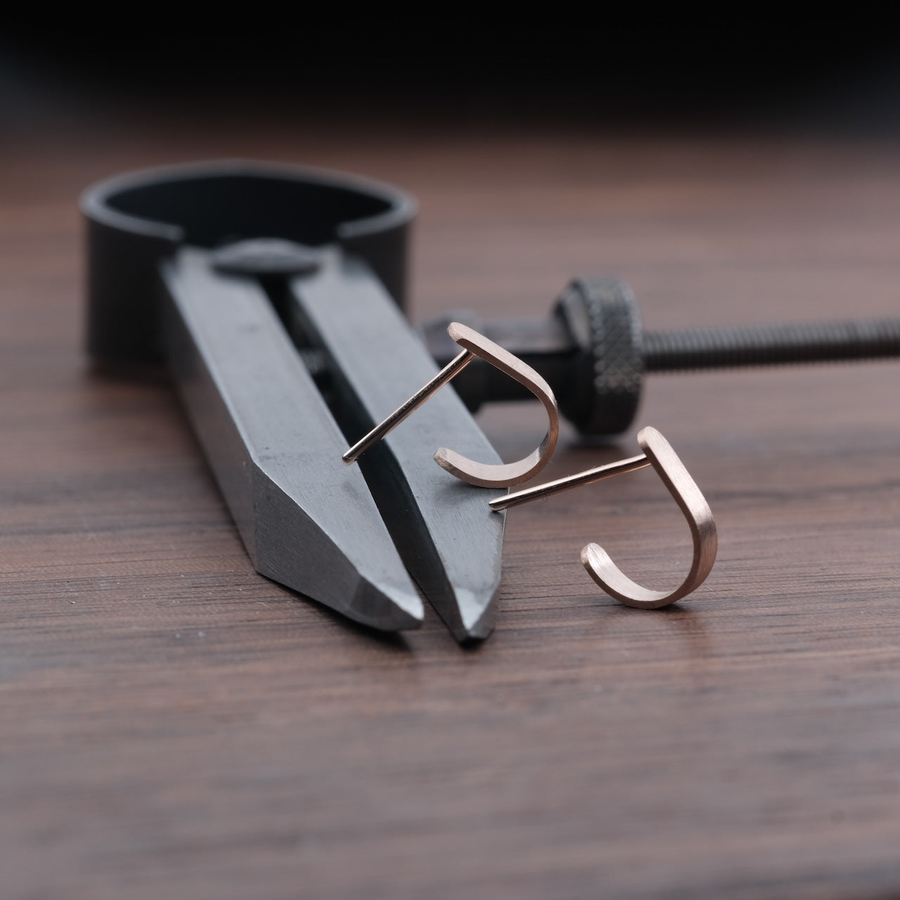 Das Bild zeigt minimalistische Ohrringe, welche auf einem Metallzirkel liegend präsentiert werden. Die Ohrringe sind aus Rose Gold.