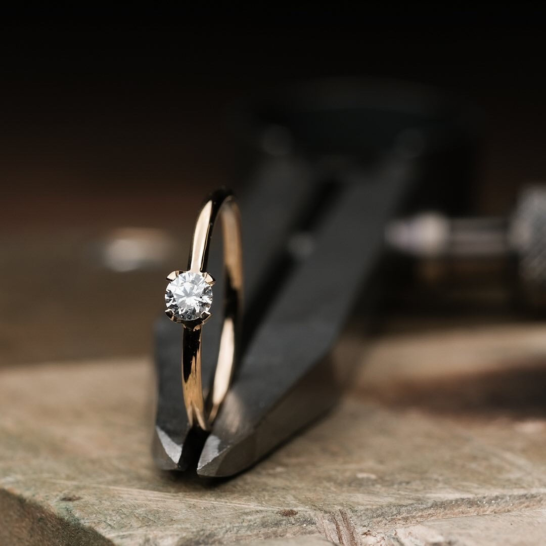 Das Foto Zeit einen Brillantring aus Gelb Gold, welcher einen Brillanten in einer vier krappen Fassung beeinhaltet.
Der Ring ist poliert. Es handelt sich um eine Macro Fotografie des eingesetzten Diamanten und dessen Fassung.