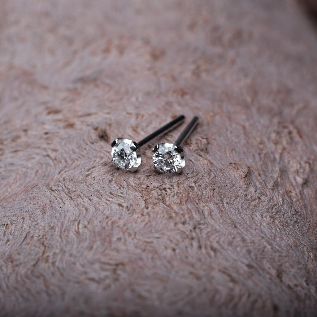 Das Bild zeigt zwei Platin Ohrringe. Sie sind mit jeweils einem Brillant besetzt. Das Set wird auf einem Holz Untergrund präsentiert.