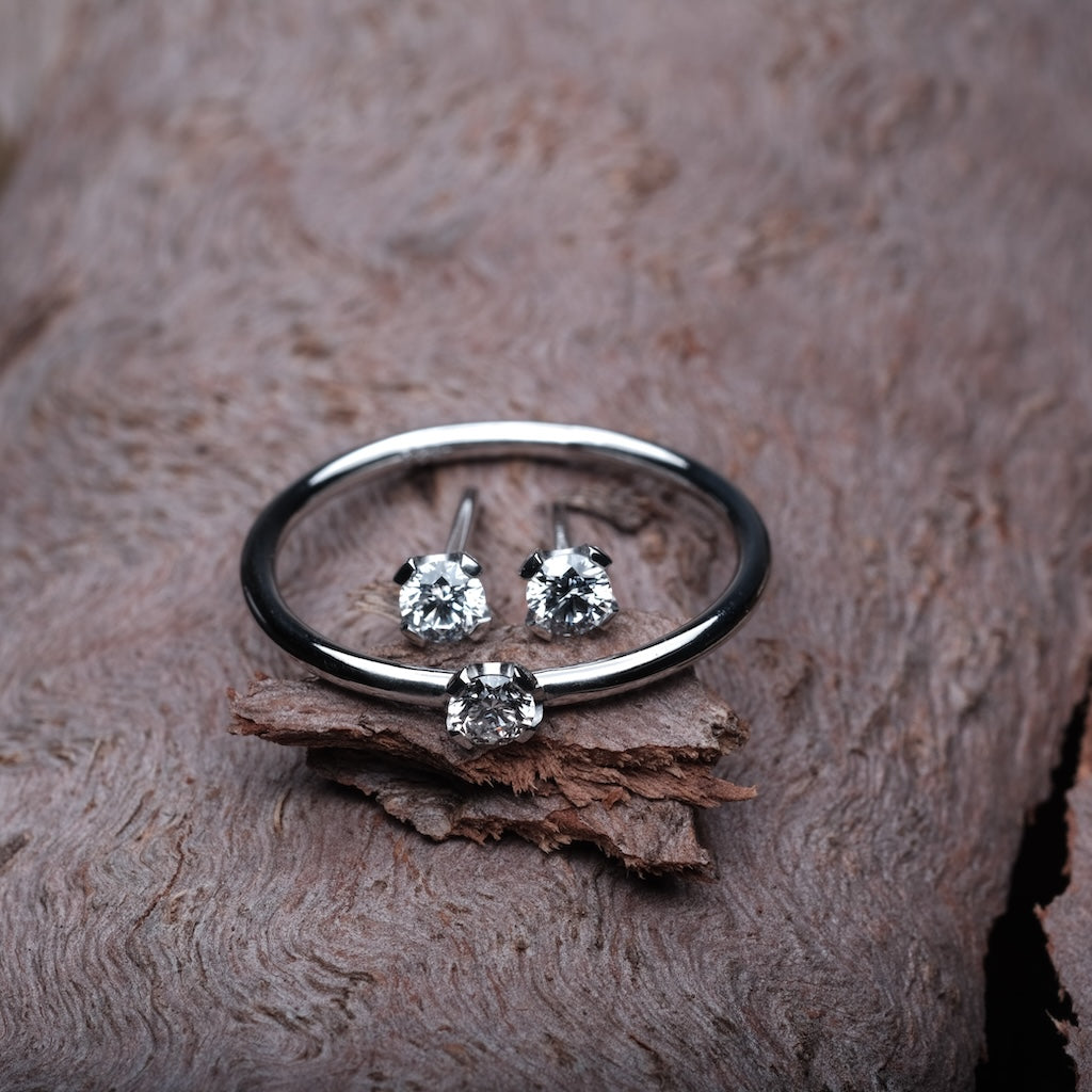 Das Bild zeigt ein Set mit einem Platin Ring und zwei Platin Ohrringen. Ring und Ohrringe sind mit jeweils einem Brillant besetzt. Das Set wird auf einem Holz Untergrund präsentiert.