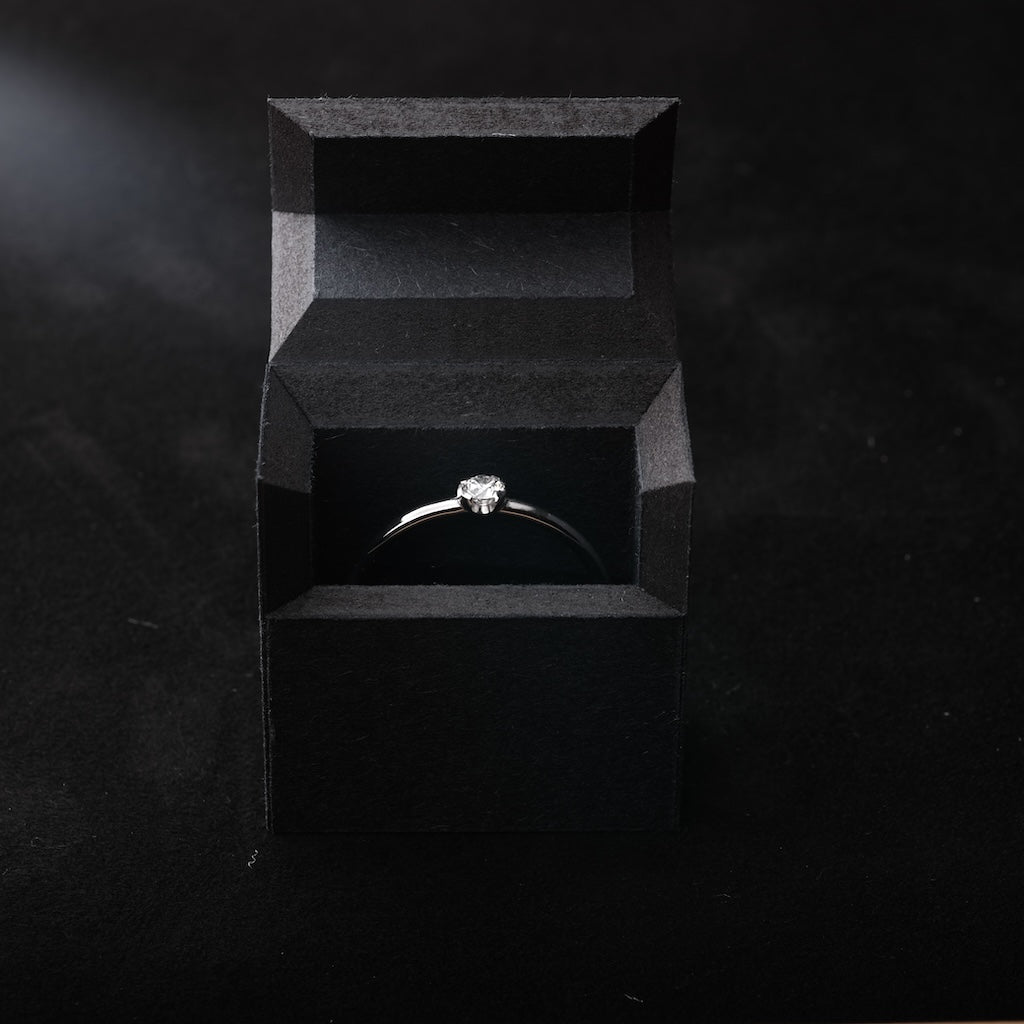 Das Bild zeigt einen Platin Ring. Dieser ist mit einem Brillant besetzt. Der Ring wird in einer Ring Schachtel präsentiert.