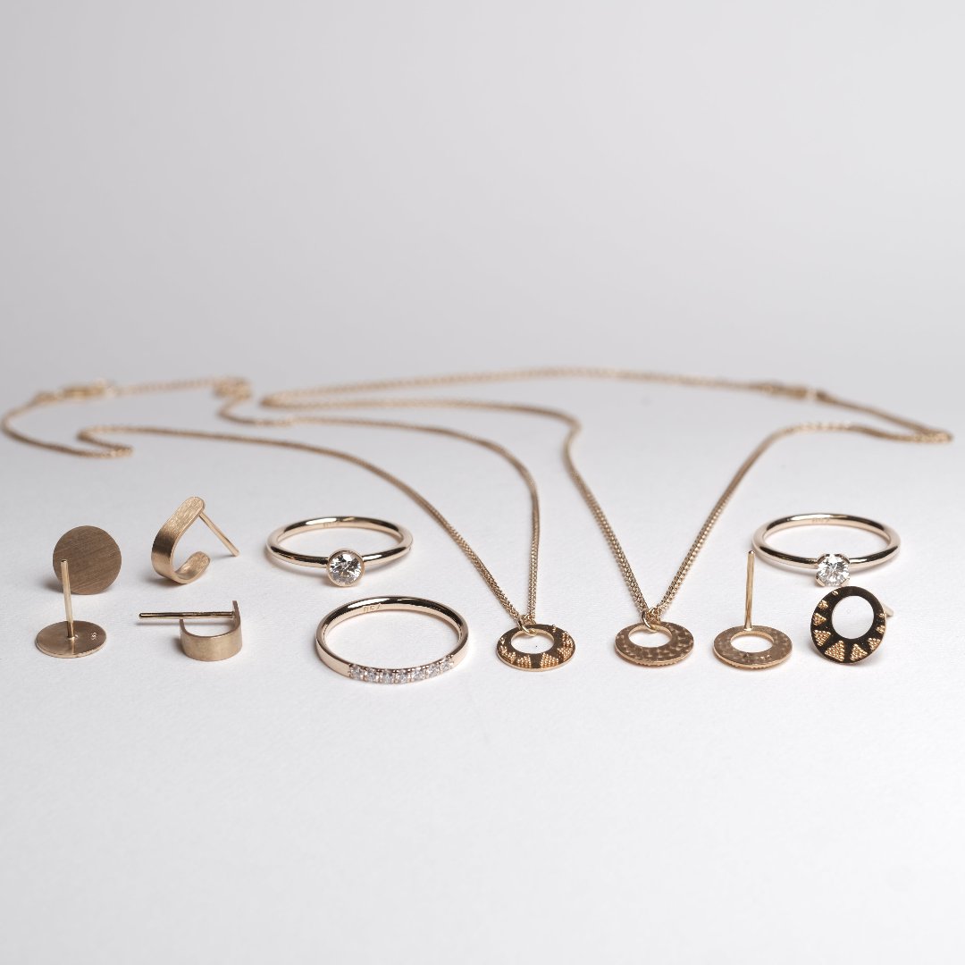 Ein Portfolio an verschiedenen echtgold Schmuckstücken, welche in zwei Reihen auf einem hellen Untergrund liegend präsentiert werden. Das Bild zeigt ein Portfolio, aus dem mit dem Geschenkegutschein beispielsweise eines der Schmuckstücke erworben werden kann.