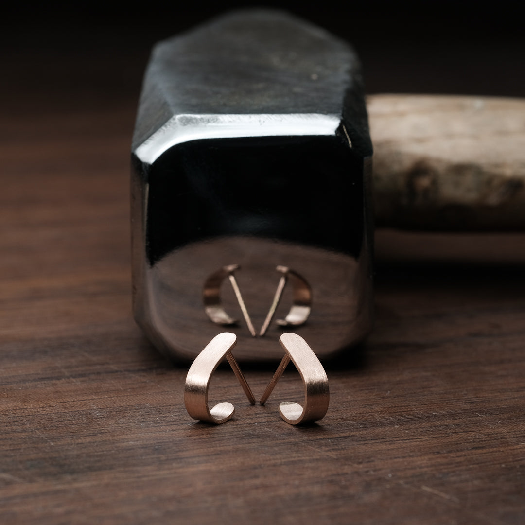 Das Bild zeigt minimalistische Ohrringe, welche vor einem Hammerl liegend präsentiert werden. Die Ohrringe sind aus Rose Gold.