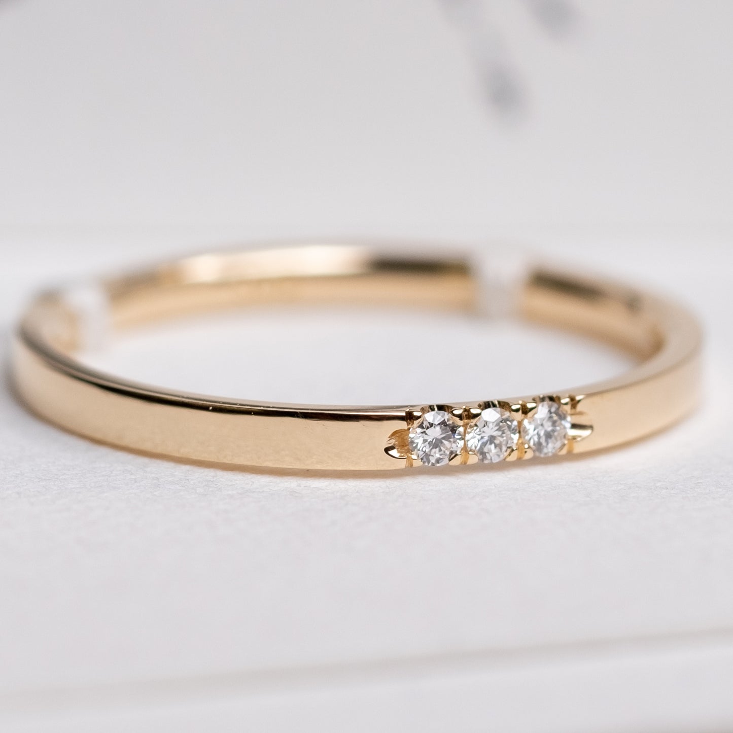 Das Bild zeit einen Brillantring aus Gelbgold, mit drei in Reihe gefassten Brillanten. Der Ring ist auf einem hellen Papieruntergrund präsentiert.