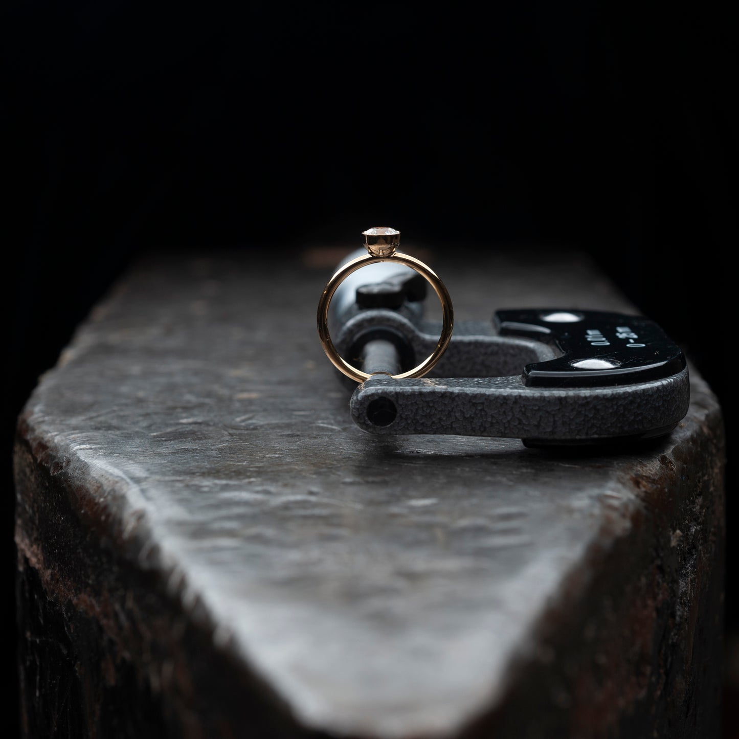 Der Ring stehend auf einem massiven Amboss. Gehalten von einer Mikrometermessschraube.