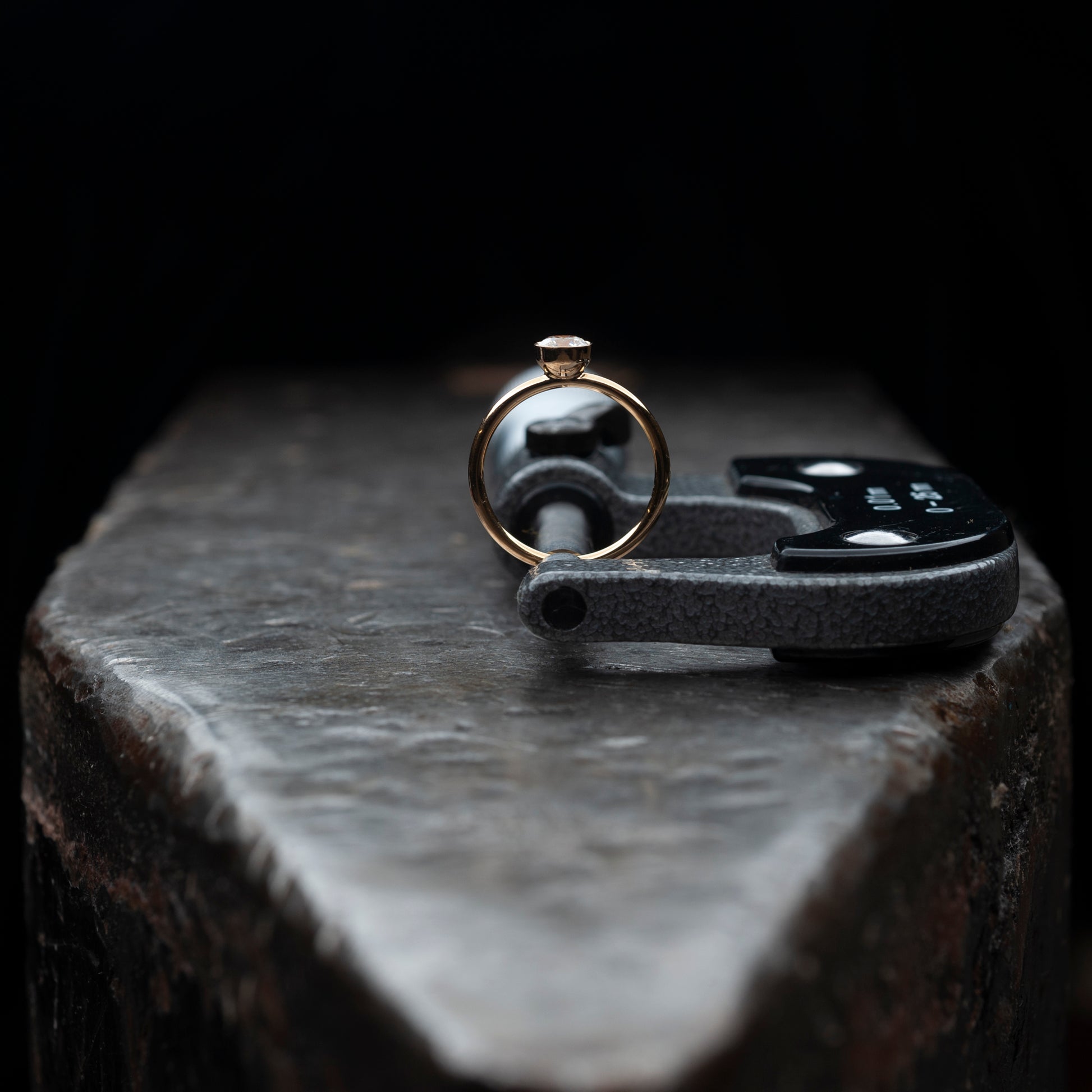 Der Ring stehend auf einem massiven Amboss. Gehalten von einer Mikrometermessschraube.