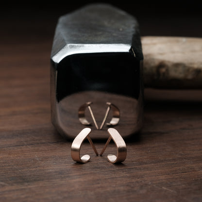 Das Bild zeigt minimalistische Ohrringe, welche vor einem Hammerl liegend präsentiert werden. Die Ohrringe sind aus Rose Gold.