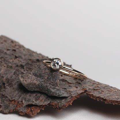 Das Bild zeigt den Brillant Ring aus der Produktbeschreibung. Es zeigt einen Gold Ring weicher mit einem Brillant besetzt ist. Der Ring wird auf einer Holz Unterlage präsentiert.
