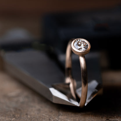 Das Foto Zeit einen Brillantring aus Rose Gold, welcher einen 0,25ct. großen Brillanten in Zargenfassung beeinhaltet.
Der Ring ist mattiert und wird eingeklemmt in einem Messschieber präsentiert.