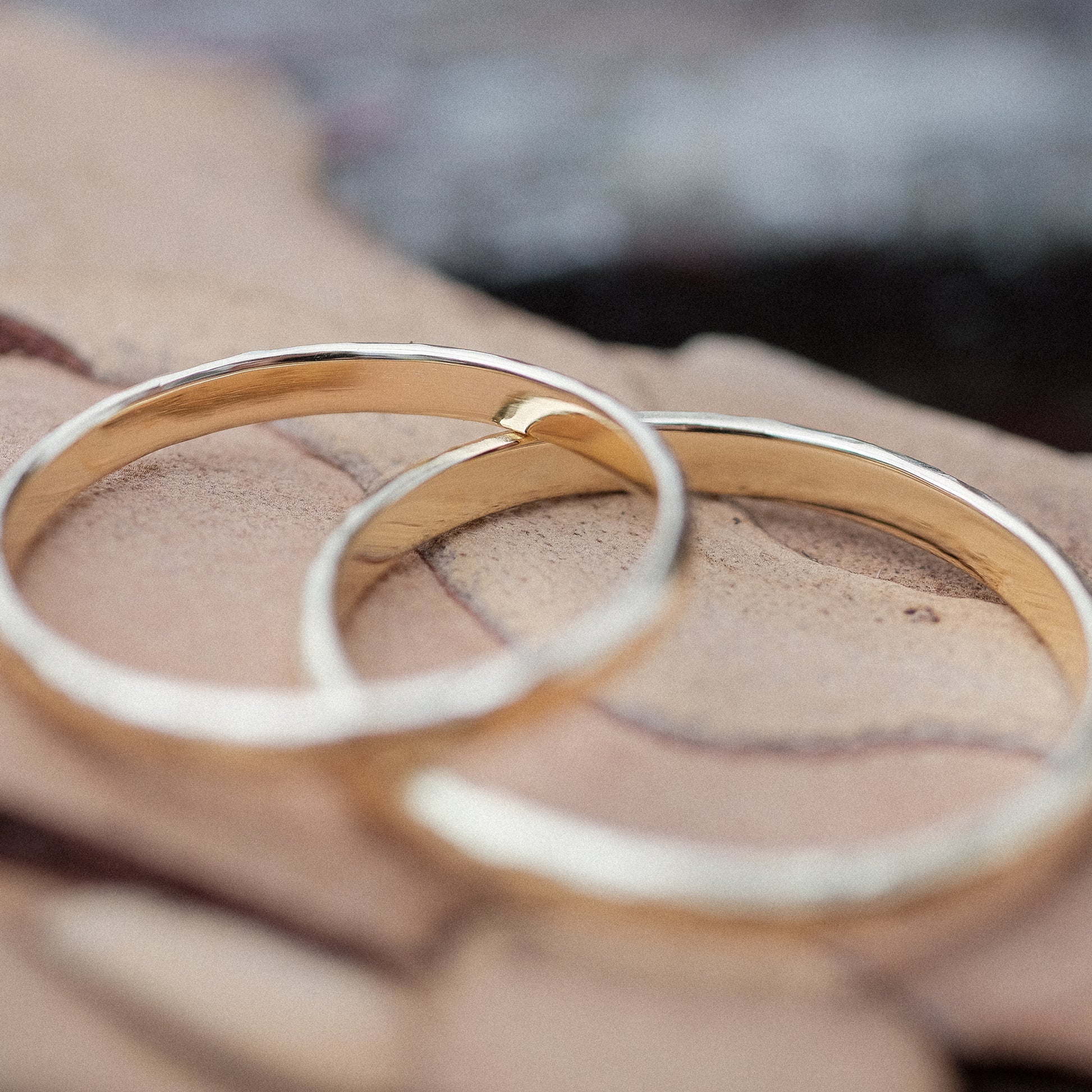 Das Bild zeigt feine Gold Eheringe welche außen halbrund und gehämmert sind und innen Flach und poliert sind. Sie werden auf einer Holzoberfläche liegend präsentiert. 